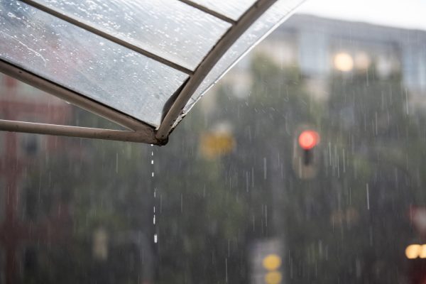 Heavy rain is dripping from the roof while a red traffic light shines in the background. Stormy weather in the urban city of Munich